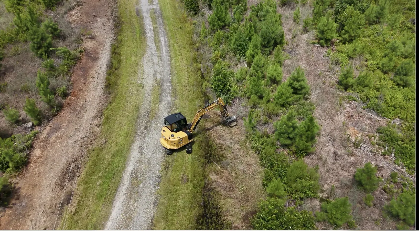 Forestry mulcher on a cleared wooded lot with logs stacked to the side